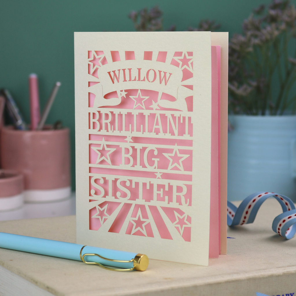 Card with 'Willow, Brilliant Big Sister' text on a desk with stationery items.