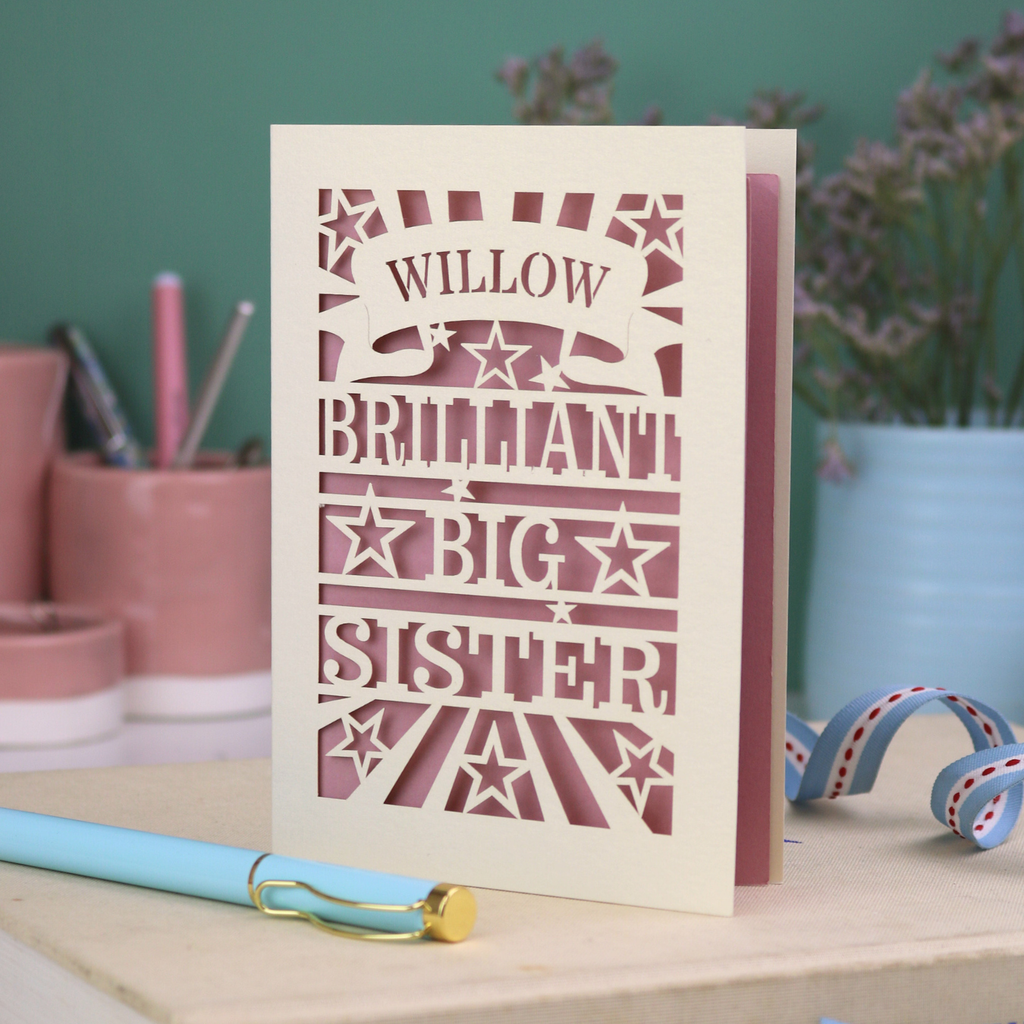 Card with 'Willow Brilliant Big Sister' text on a desk with stationery items.