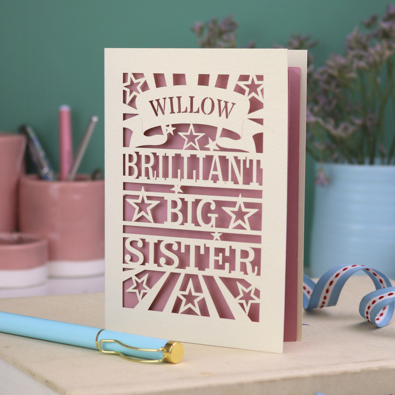 Card with 'Willow Brilliant Big Sister' text on a desk with stationery items.