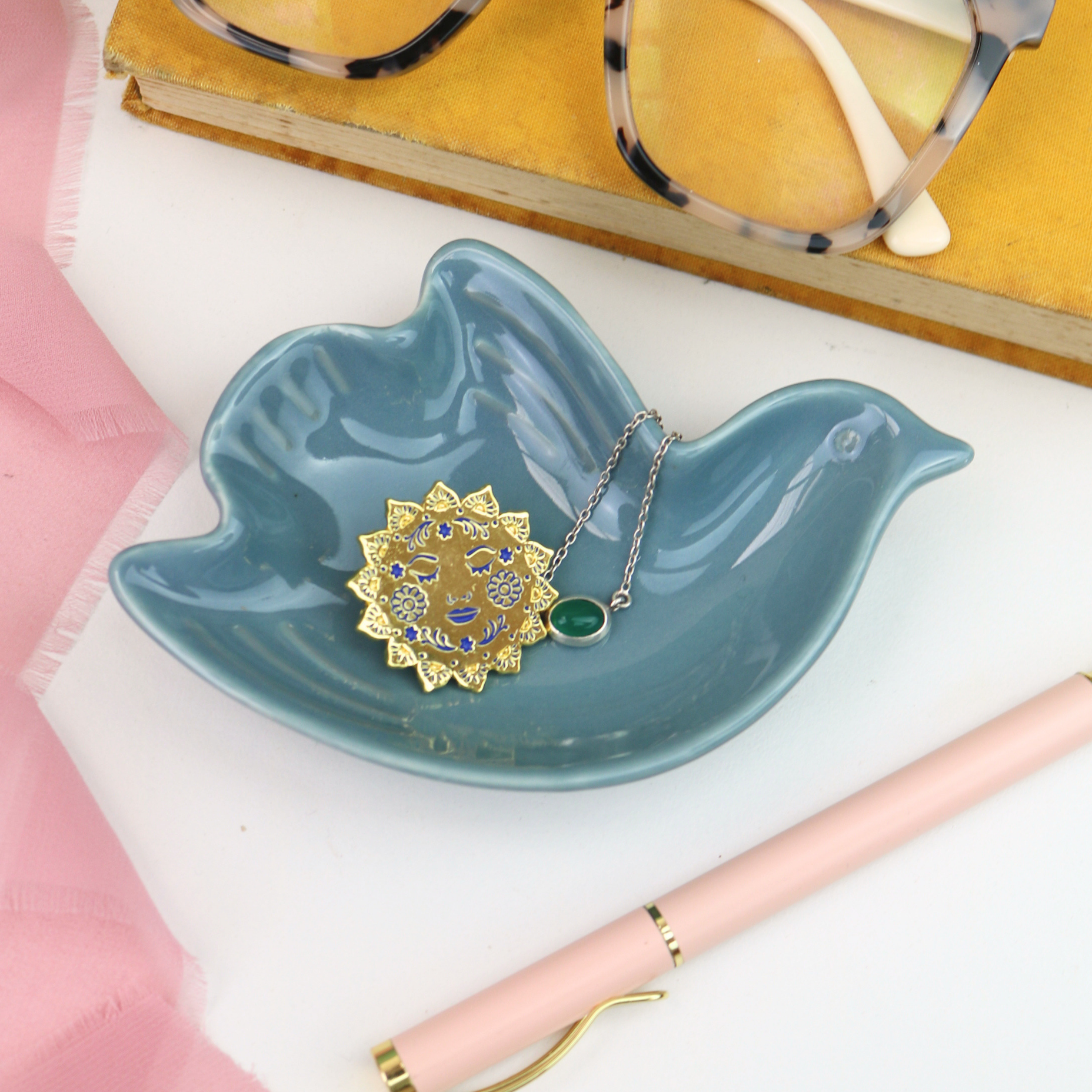 Blue ceramic bird-shaped trinket dish with jewelry on a white surface.