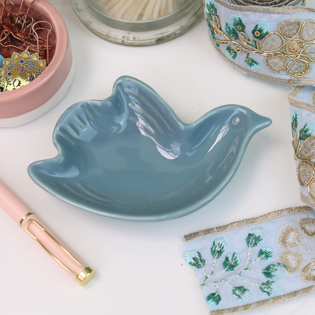 Blue ceramic bird-shaped dish on a white surface with decorative items.