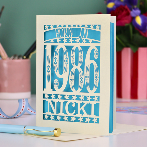 Personalized birthday card with 'Born in 1986 Nicki' design on a desk with stationery items.