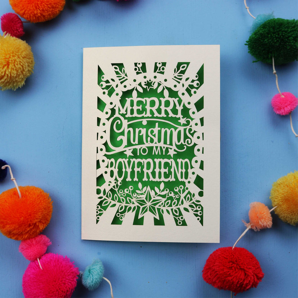 Papercut Boyfriend Christmas card with 'Merry Christmas to my boyfriend' text on a blue background with colourful pom-poms.