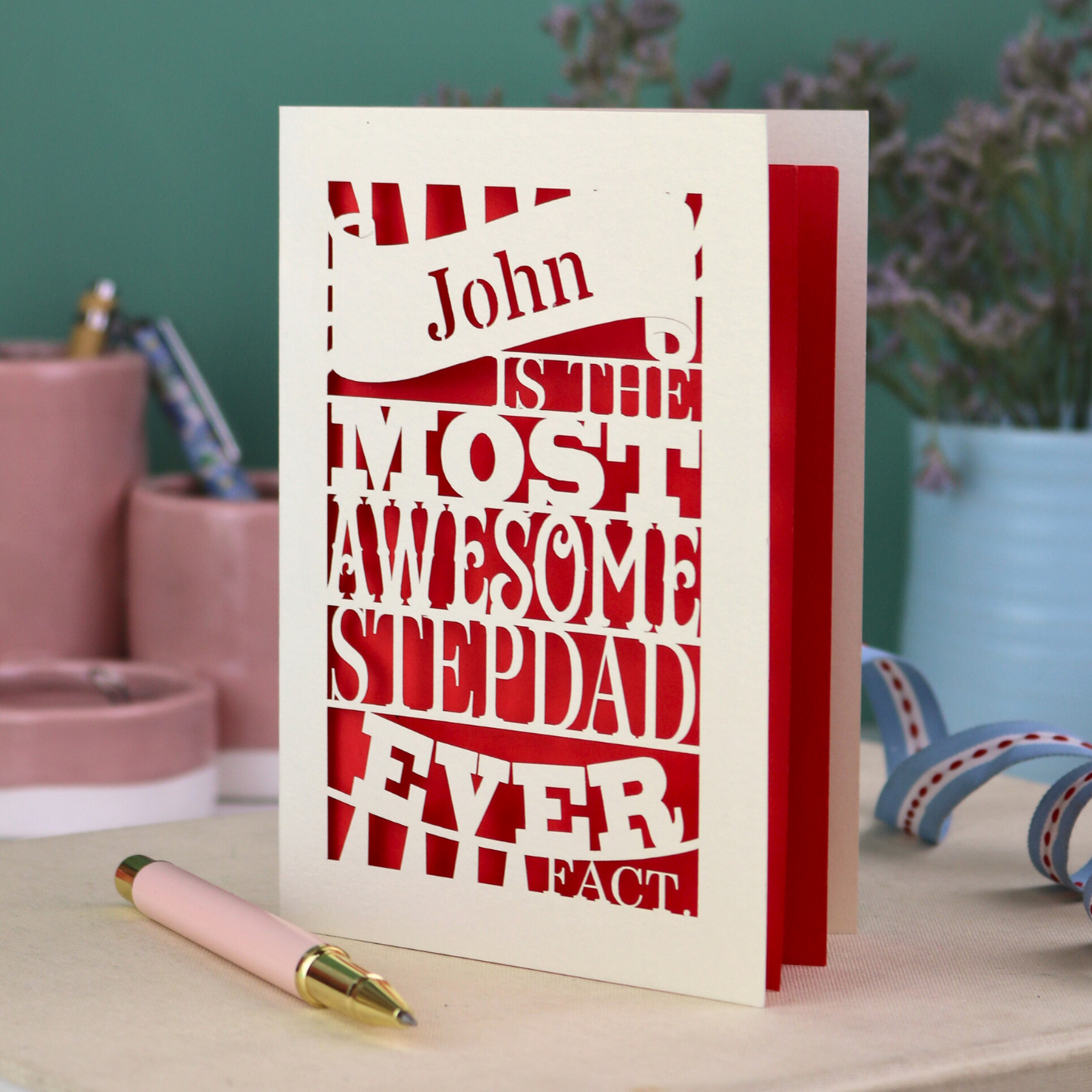Laser cut Stepdad Card with personalized text, "John is the most awesome stepdad ever. Fact." on a table with decorative items