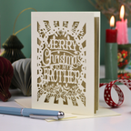 A handmade brother Christmas card reading 'MERRY Christmas TO MY BROTHER'. The card is displayed on a tabletop with a blue pen in the foreground and a lit candle in the background, creating a cosy holiday atmosphere.