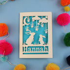 Decorative birthday card with cut-out rabbits and 'Hannah' text on a blue background with colourful pom-poms.