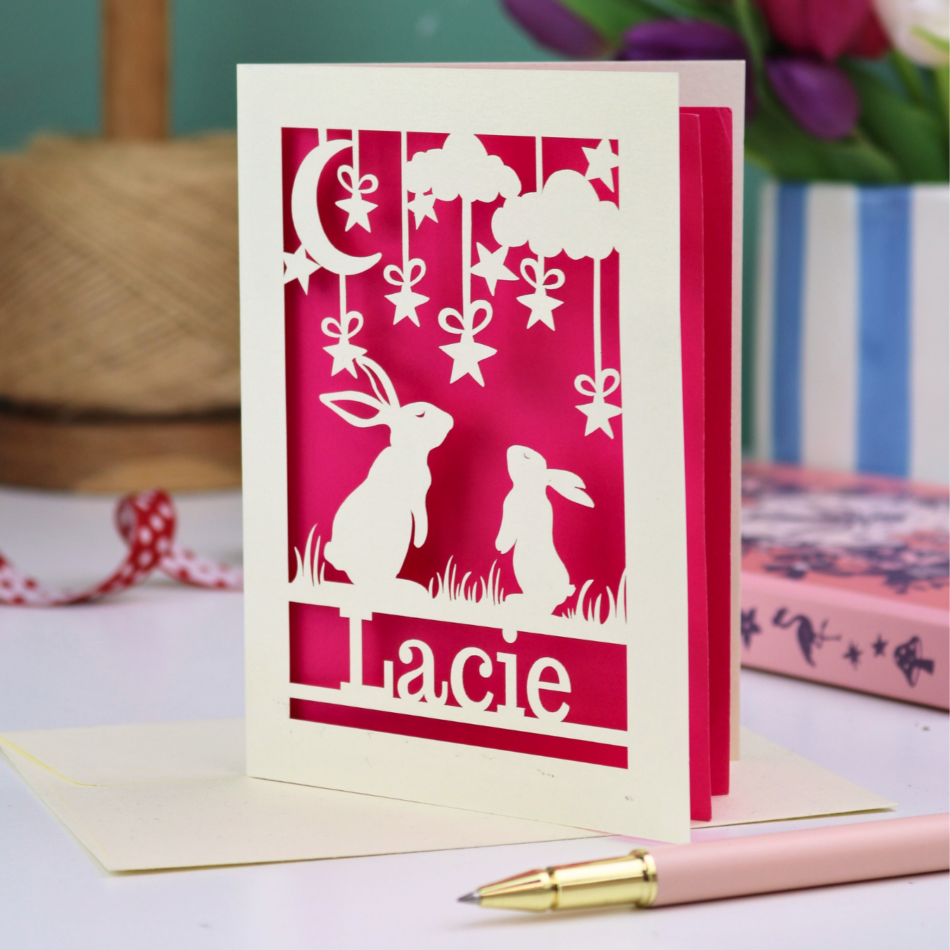 Personalised Special Birthday Card with laser cut rabbit design and 'Lacie' text on a pink background, with a pen and flowers in the background.