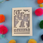 Decorative birthday card with cut-out rabbits and 'Hannah' text on a blue background with colourful pom-poms.