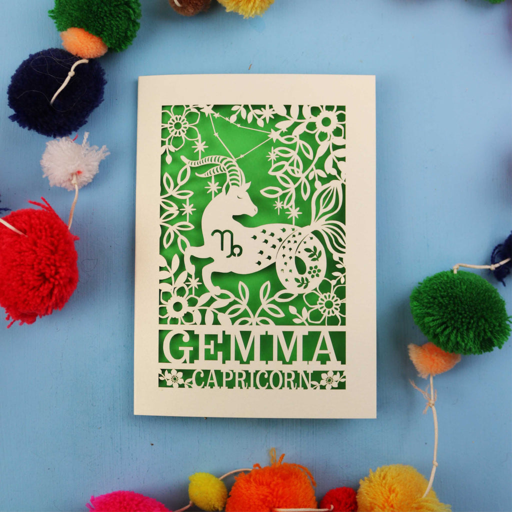 Decorative birthday card with Capricorn zodiac symbol on a blue background with colourful pom-poms.