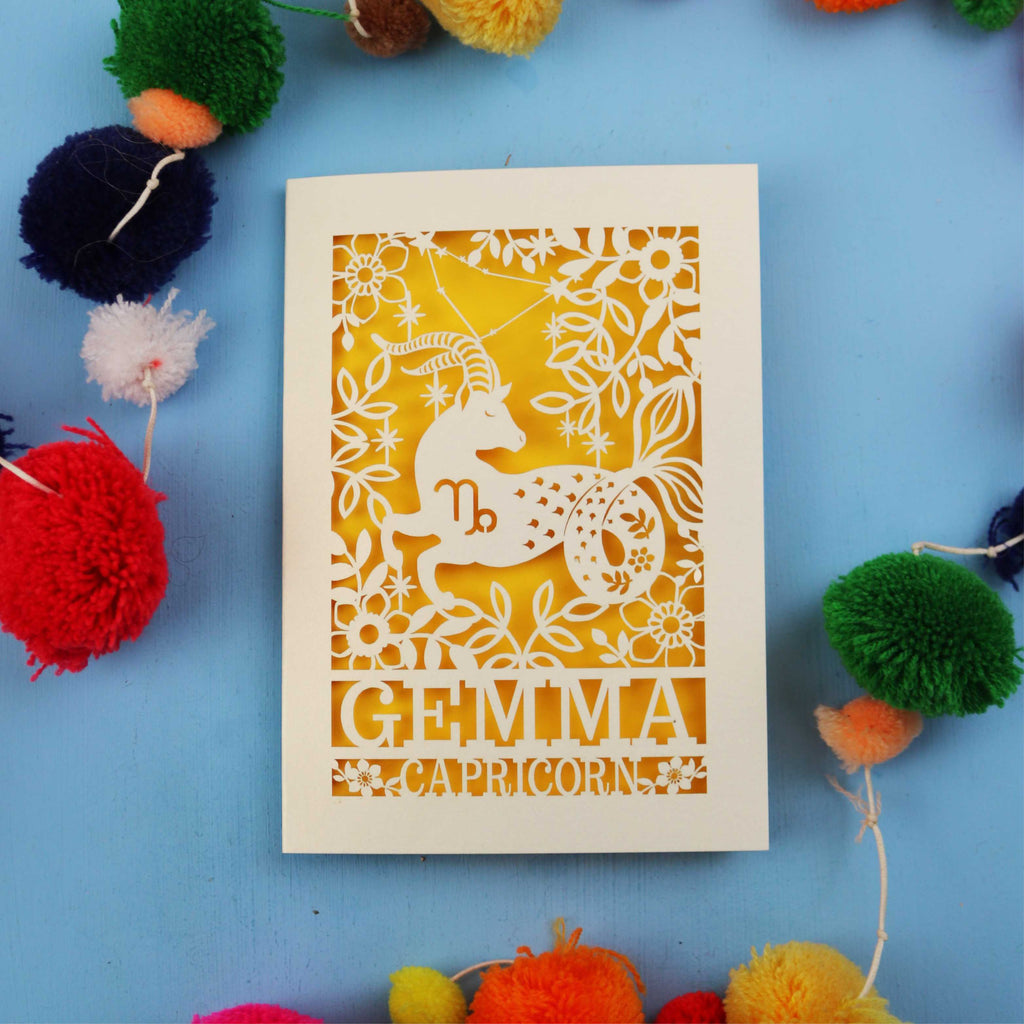 Decorative birthday card with Capricorn zodiac symbol on a blue background with colourful pom-poms.