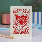 A laser cut husband valentines card with floral design on a green background