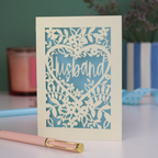 A laser cut husband valentines card with floral design on a green background