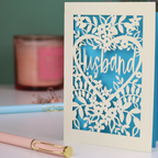 A laser cut husband valentines card with floral design on a green background