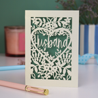 A laser cut husband valentines card with floral design on a green background