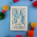 Decorative 1st birthday card with cut-out design of a cat and 'Holly' text, surrounded by colourful pom-poms on a blue background.