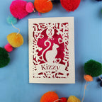 Decorative birthday card with cut-out design of a cat and text 'Kizzy' on a blue background with colourful pom-poms.