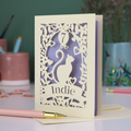 A cream laser cut birthday card with cat design and personalised with '7' in a balloon and the name of the recipient, 'Indie' in a banner