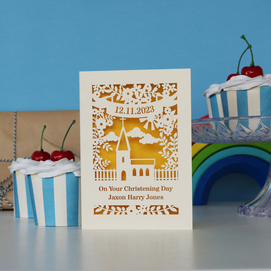 A cream Christening card with a church and text, and a yellow paper insert behind.