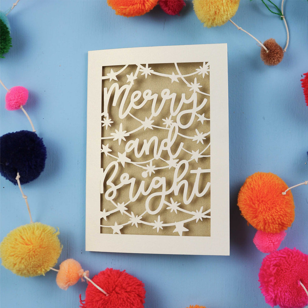 Decorative card with 'Merry and Bright' text surrounded by colourful pom-poms on a blue background