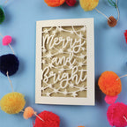 Decorative card with 'Merry and Bright' text surrounded by colourful pom-poms on a blue background