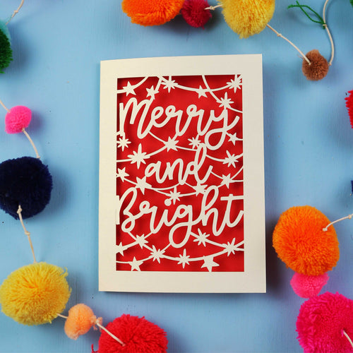Decorative card with 'Merry and Bright' text surrounded by colourful pom-poms on a blue background