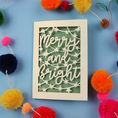 Decorative card with 'Merry and Bright' text surrounded by colourful pom-poms on a blue background