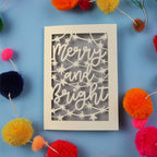 Decorative card with 'Merry and Bright' text surrounded by colourful pom-poms on a blue background