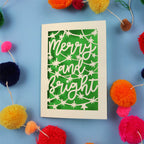 Decorative card with 'Merry and Bright' text surrounded by colourful pom-poms on a blue background