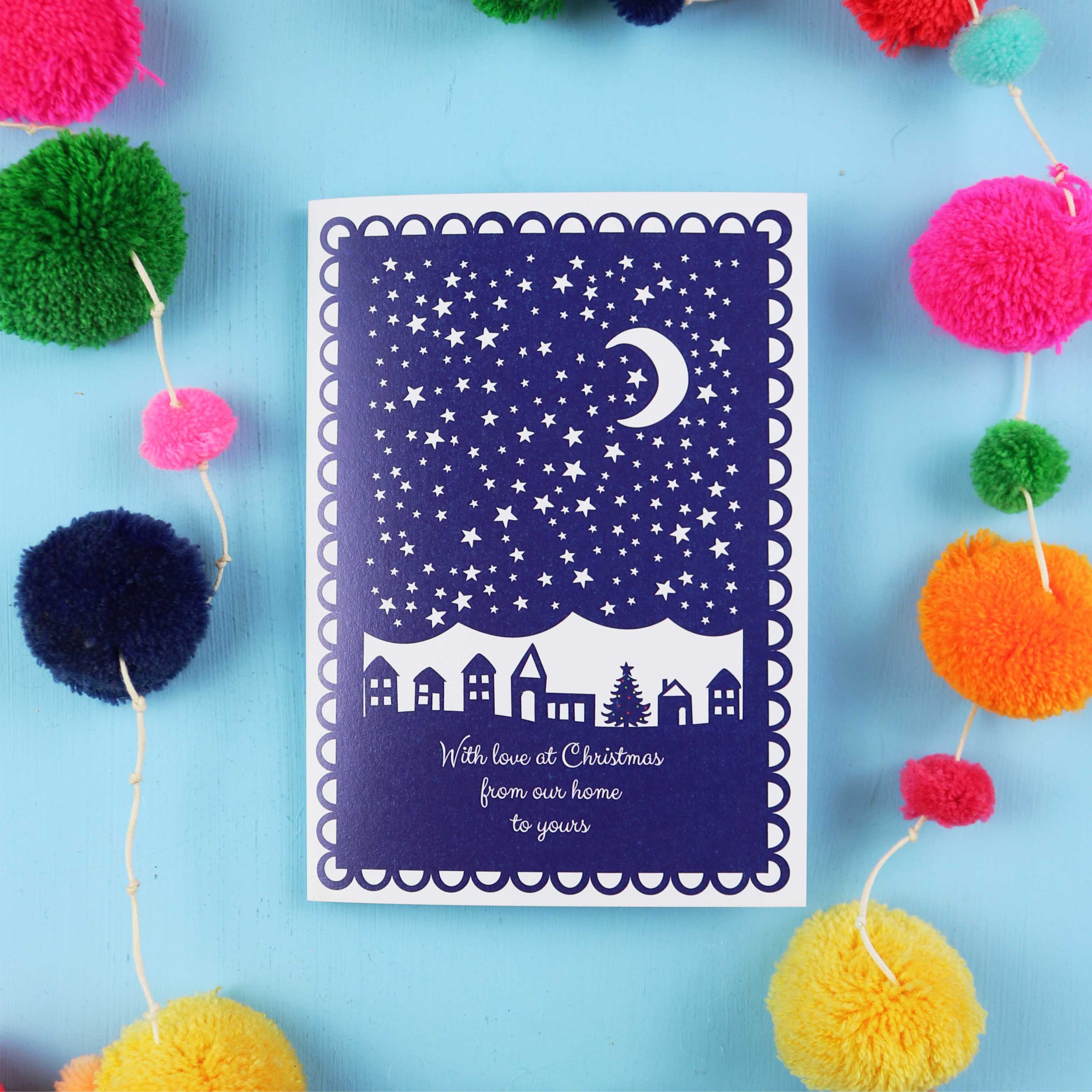 Navy blue Christmas card with white design on a blue background with colourful pom-poms.