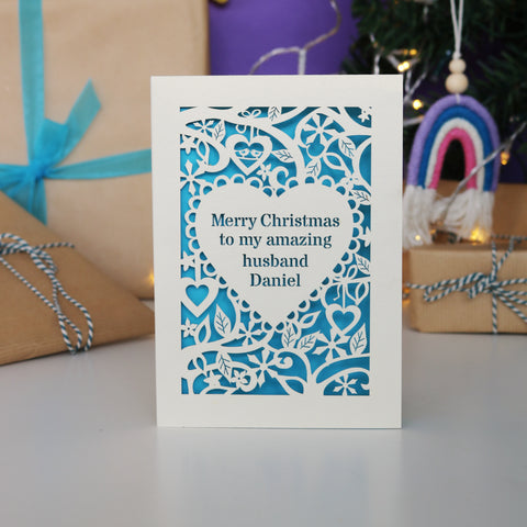 A personalised card for Christmas. Card has text  "Merry Christmas to my amazing husband Daniel" inside a heart shape, with a border of hearts, flowers and snowflakes. - A5 / Cream / Peacock Blue