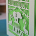 A laser cut birthday card with circus big top design, "Happy Birthday" and a name, with an age cut out.
