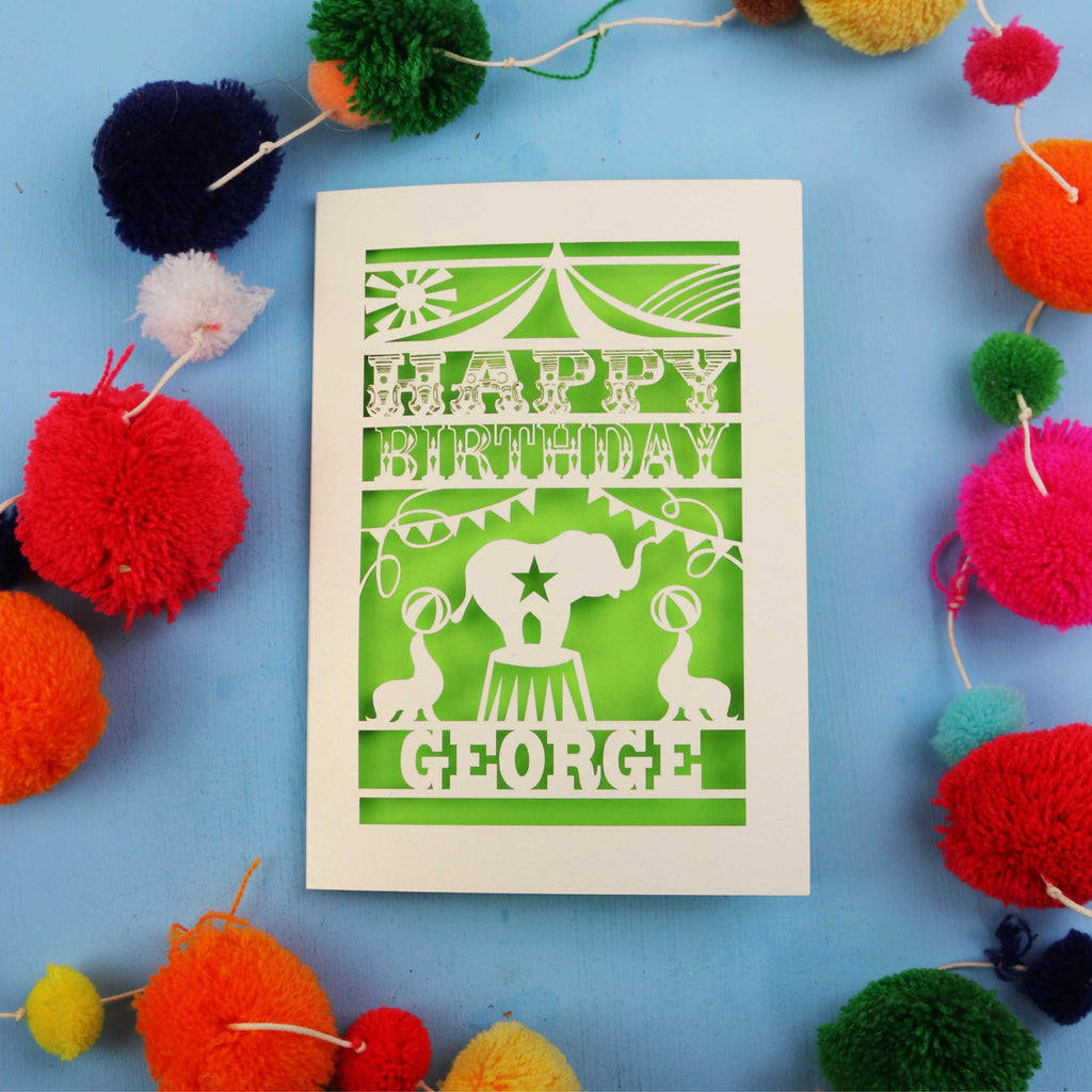 Personalised Circus Birthday card with 'Happy Birthday George' text on a blue background with colourful pom-poms.