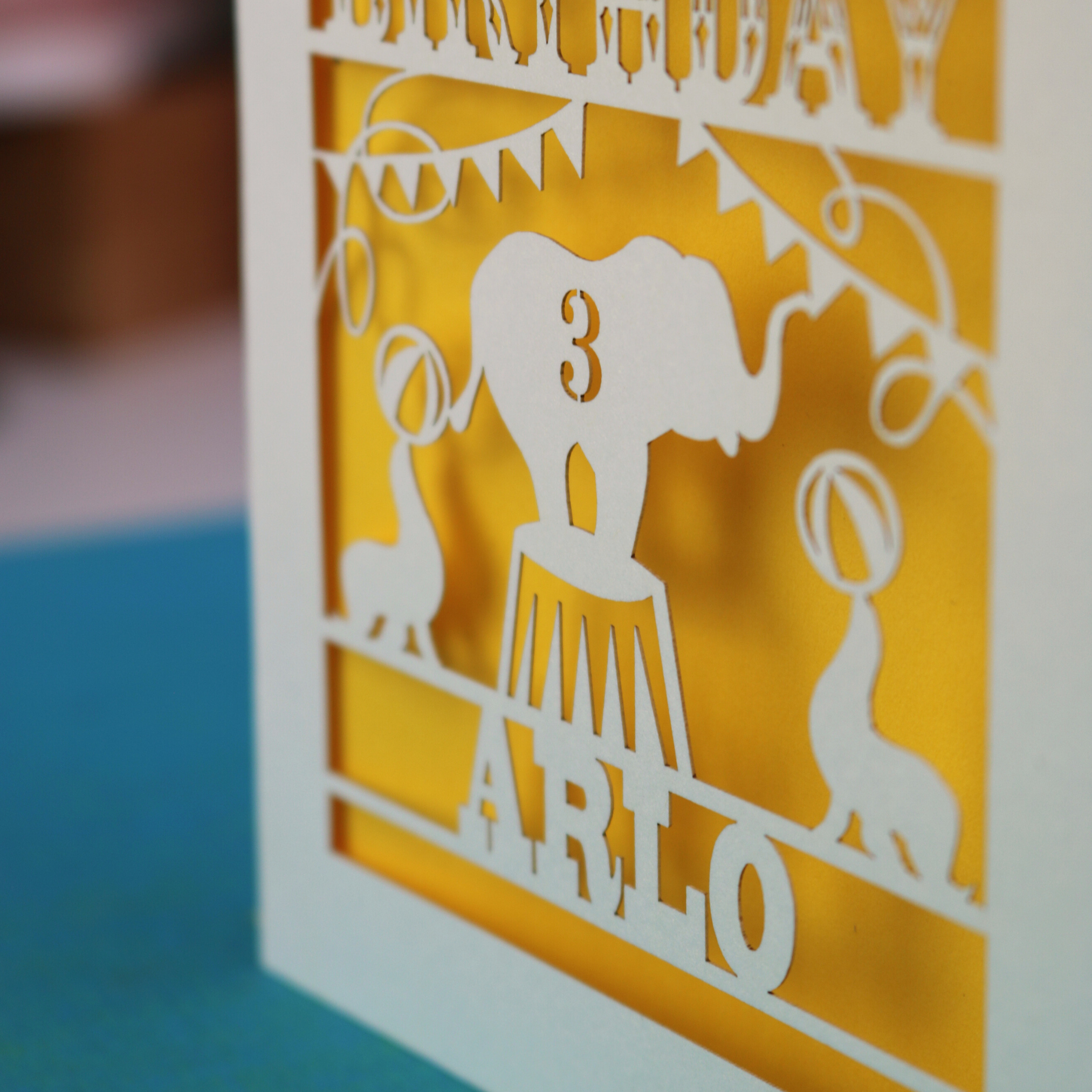 A laser cut birthday card with circus big top design, "Happy Birthday" and a name, with an age cut out.