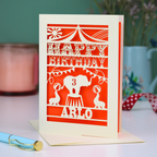 Birthday card with orange circus design on a table with a candle and decorative items.