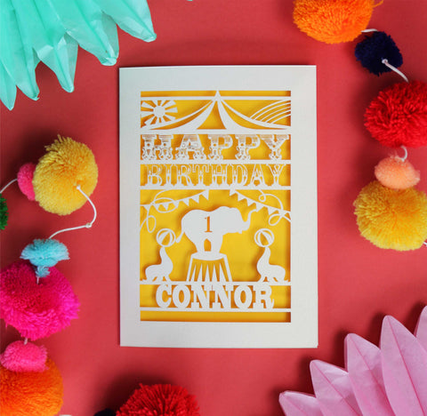Circus themed birthday card for children. Shows an elephant and seals in the big top. Lasercut from cream card and shown with a sunshine yellow background. Personalised with a name and age. - 
