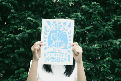 A person holding up a coffee print that says "but first, coffee" - 