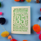 Papercut Coral anniversary Card with '35 amazing years' on a blue background with colourful pom-poms