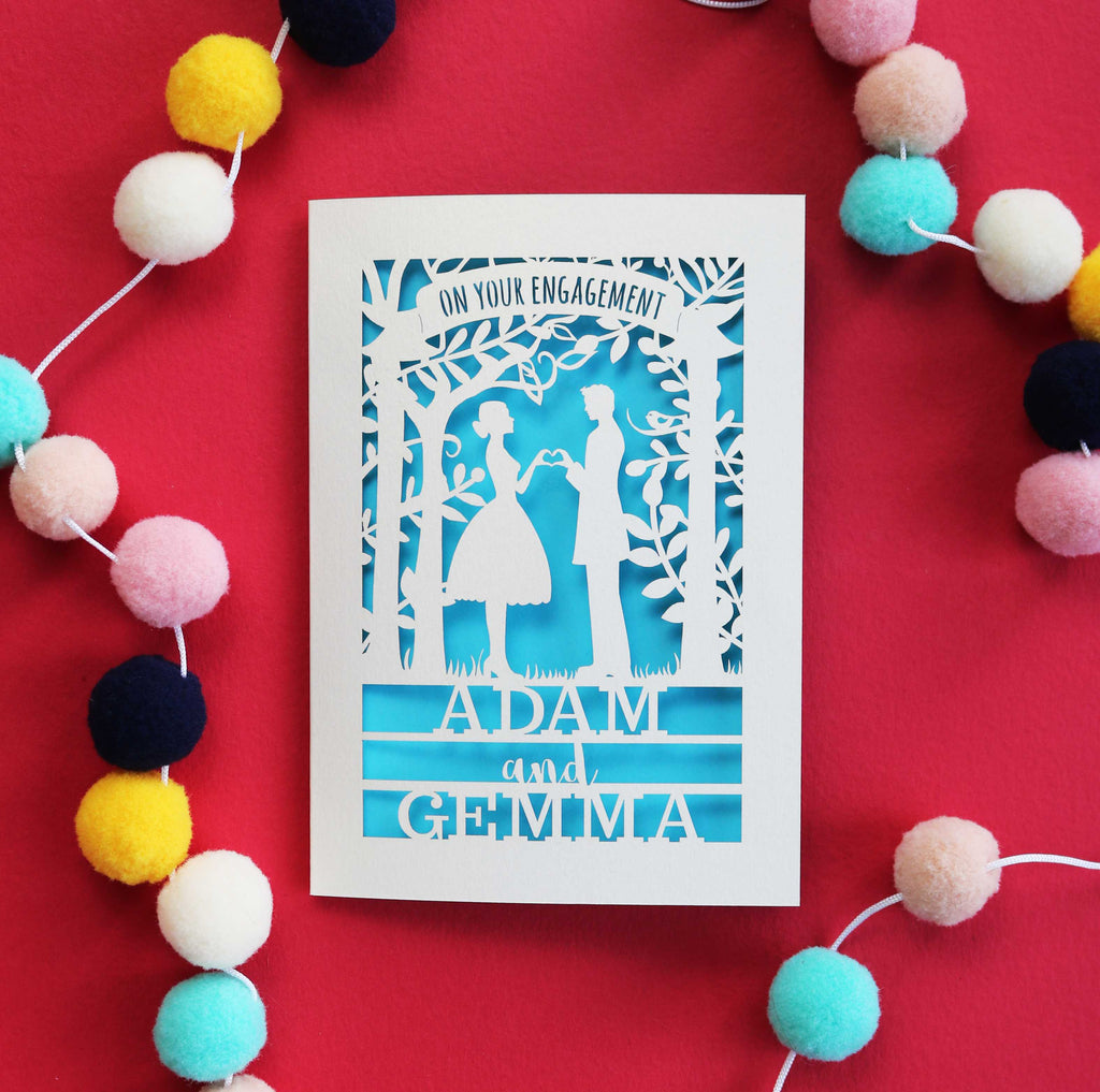 A laser cut engagement card that says "on your engagement" with the names at the bottom and silhouettes of a man and woman in the middle