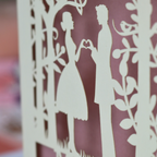  cut-out of a couple holding hands with a heart shape against a blurred background