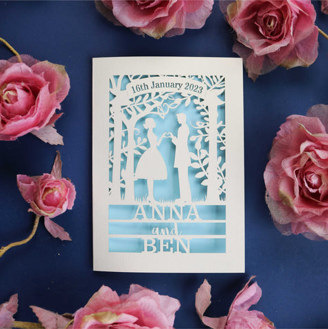 A cut out card for weddings that features the silhouettes of a couple, and is personalised with a date in a banner at the top and the names of the couple over three lines of text at the bottom - A6 (small) / Light Blue