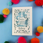 Decorative 1st birthday card with 'Eden' on a blue background with colourful pom-poms