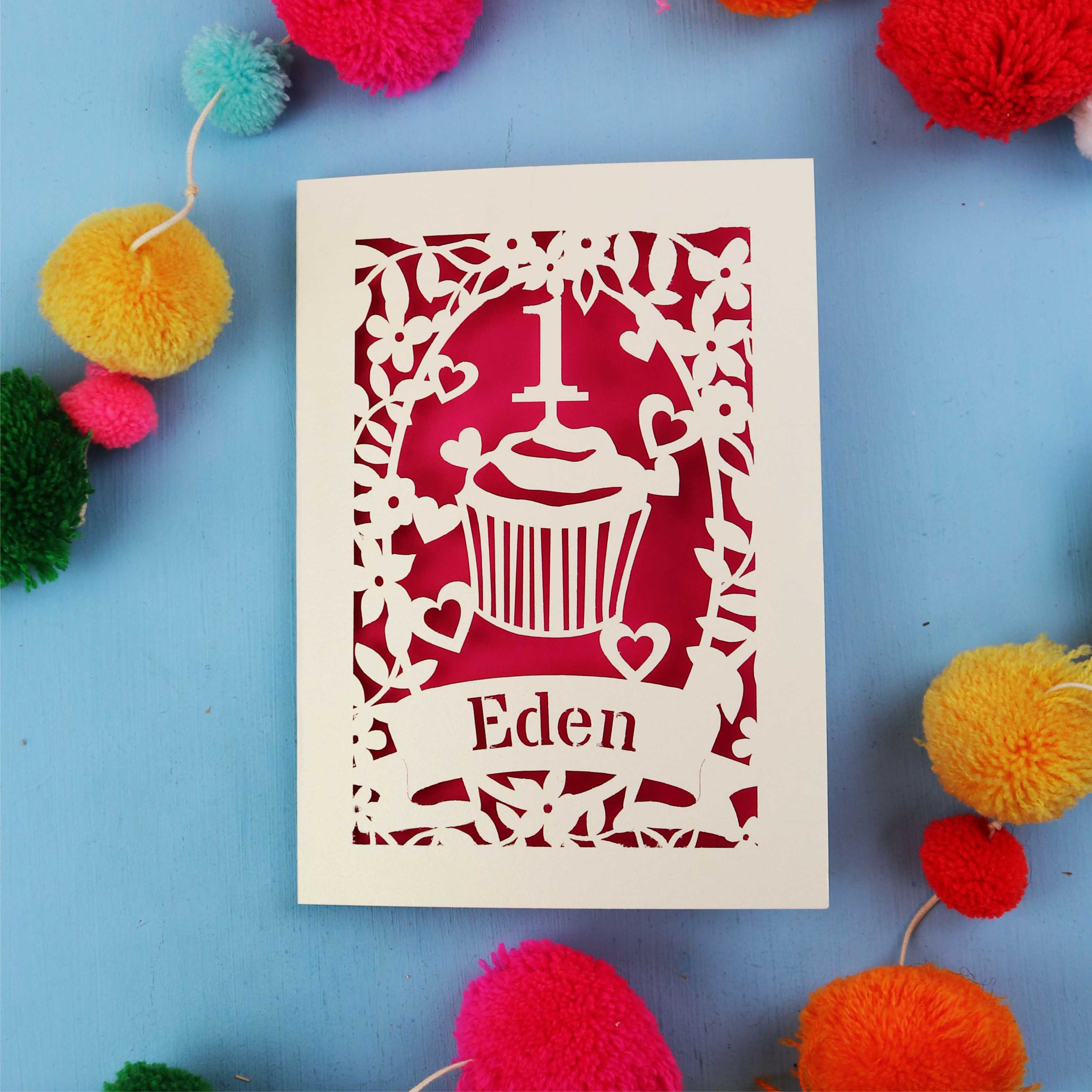 Keepsake 1st birthday card with 'Eden' on a blue background with colourful pom-poms