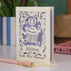 A personalised 60th birthday card with laser cut cupcake design and the age '60', with the name 'Alison' cut out of a banner in a laser cut stencil font