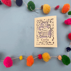Decorative laser cut birthday card with '50' and 'Carla' on a blue background with colourful pom-poms.