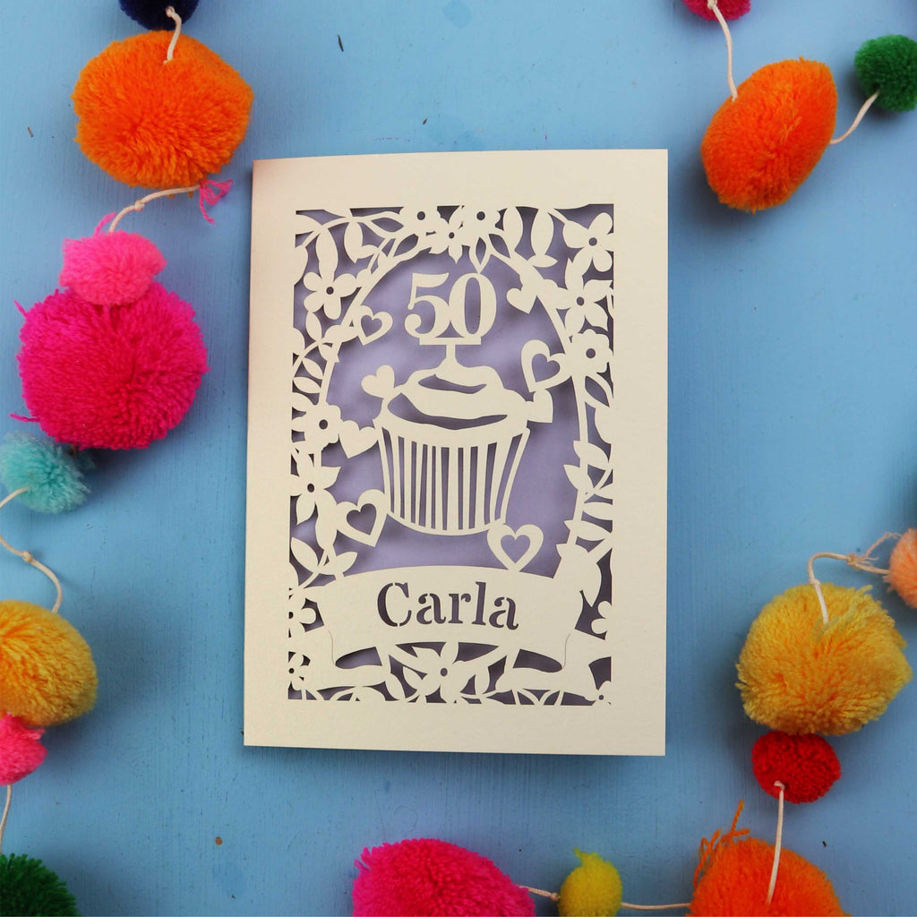 Decorative cut out birthday card with '50' and 'Carla' on a blue background with colourful pom-poms.