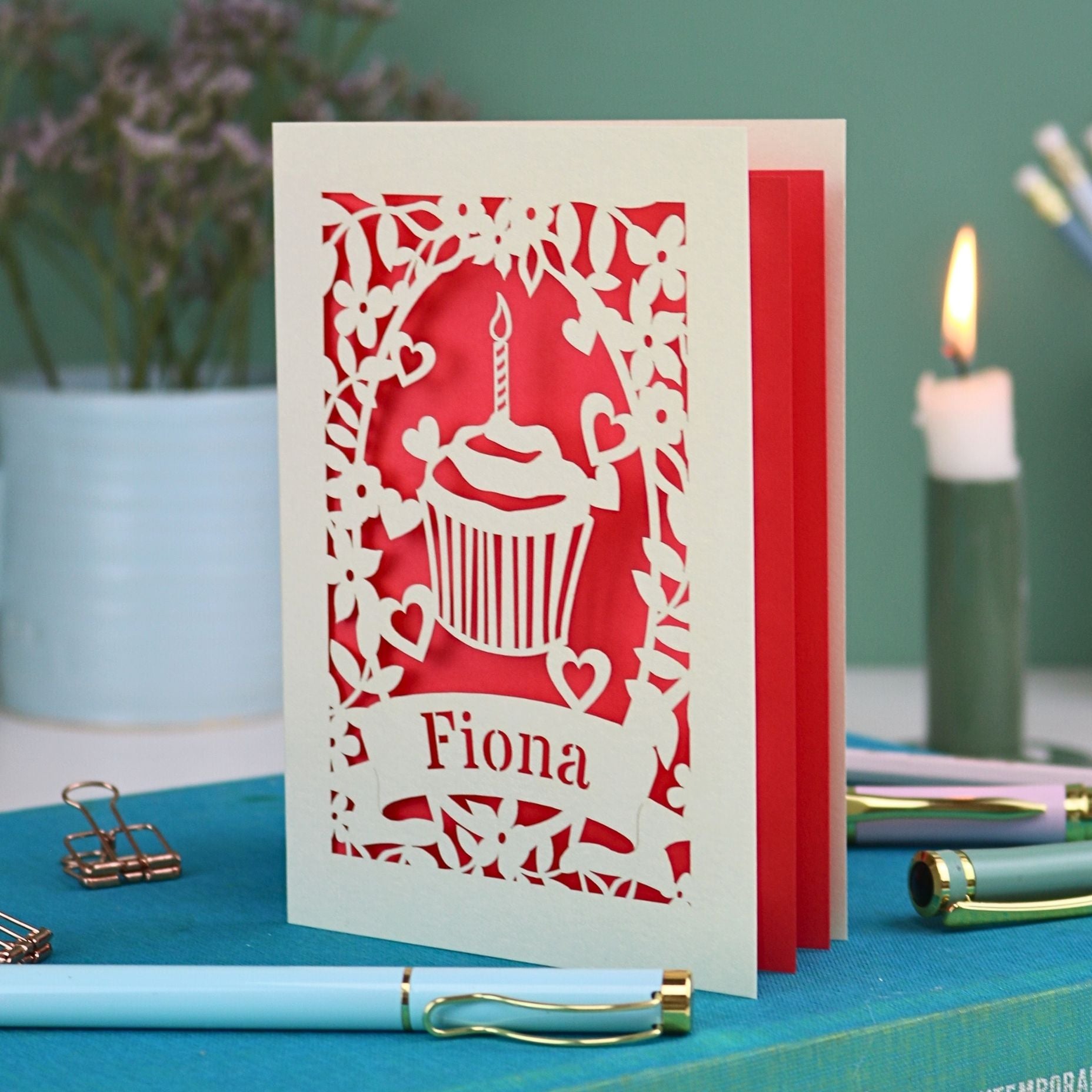 A laser cut birthday card with floral border, cupcake design and personalised with the name "Fiona" cut out of a banner shape