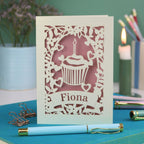 A laser cut birthday card with floral border, cupcake design and personalised with the name "Fiona" cut out of a banner shape
