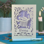 A laser cut birthday card with floral border, cupcake design and personalised with the name "Fiona" cut out of a banner shape