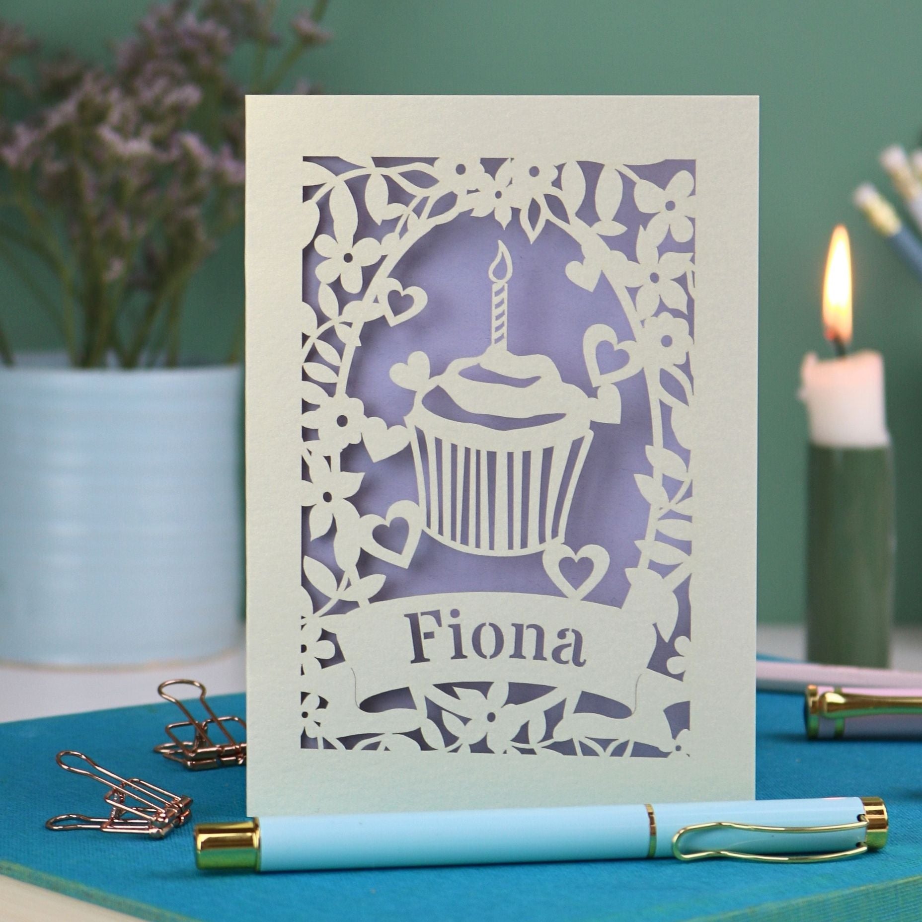 A laser cut birthday card with floral border, cupcake design and personalised with the name "Fiona" cut out of a banner shape