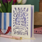 A cream and lilac laser cut personalised 60th birthday card with cupcakes on a cake stand design, the number '60' and "Happy Birthday Jenny" personalised text in cut out stencil lettering
